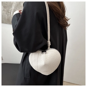 Detailed view of white heart-shaped crossbody bag with crocodile texture and double zippers