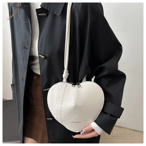Detailed view of white heart-shaped crossbody bag with crocodile texture and silver zipper