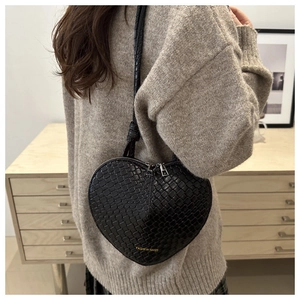 Detail of a black heart-shaped handbag with woven texture and a gold logo on the side