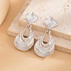 Detailed macro view of silver earrings with irregular hammered texture on travertine stone