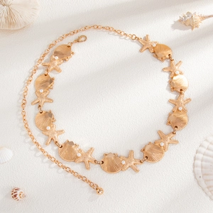 Detail of gold starfish and shell waist chain with pearls on white sand background