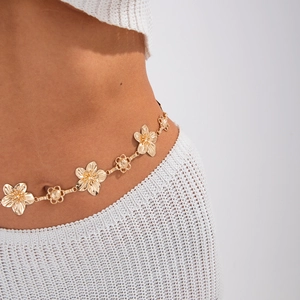Close-up of golden floral metal waist chain with intricate镂空circle links on white knitwear