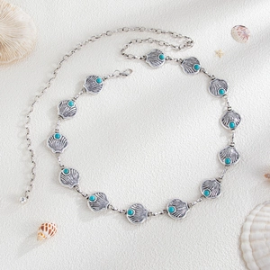 Detail of silver alloy shell waist chain with turquoise beads on white sand background