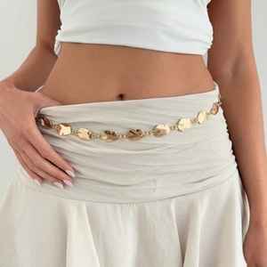 Close-up of golden hollow irregular metal waist chain on white dress