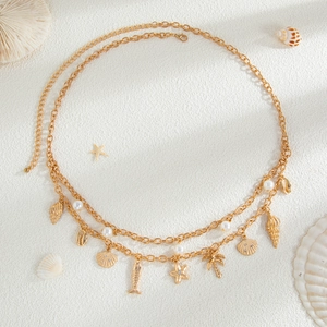Detail of layered gold waist chain with seashell, starfish pendants and pearls