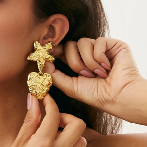 Close-up of gold irregular starfish and hammered heart drop earrings on model