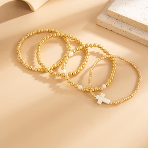 Detailansicht eines vier-teiligen goldenen Perlenarmband-Sets mit Kreuzanhänger