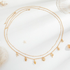 Detail of gold double-layer body chain with starfish and shell charms on beach sand