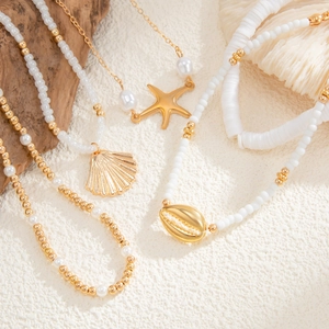 Detail of beach jewelry set featuring gold starfish, shell charms and white beads