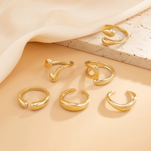 Detail of six gold lava rings with S925 engraving on a beige silk and stone background