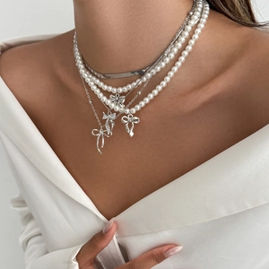 Détail de colliers superposés argentés avec perles et pendentifs nœuds en strass