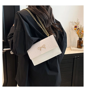 Close-up of cream crocodile pattern bag with golden bow hardware and chain strap