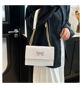Detail of white woven flap shoulder bag with gold bow clasp and chain strap on a model