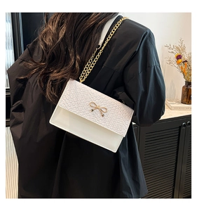 Detail of cream woven leather shoulder bag with gold bow clasp and metal chain strap