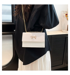 Detail of white crocodile pattern bag with golden bow clasp and metallic chain strap