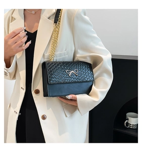 Detail of black crocodile texture bag with golden bow buckle and chain shoulder strap