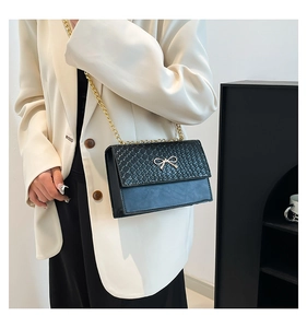 Detail of black faux stone texture handbag featuring a golden bow buckle and chain strap