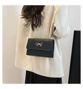 Close-up of black crocodile pattern bag with golden bow hardware and chain strap
