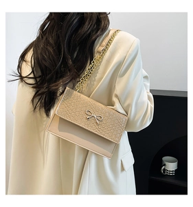 Détail du sac beige avec fermoir nœud doré sur rabat en cuir tressé porté par un mannequin
