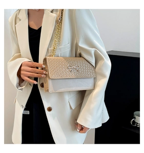 Detailed close-up of beige crossbody bag featuring woven texture and golden bow clasp