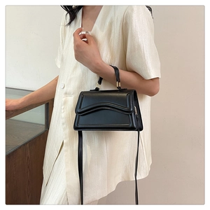 Détail du petit sac carré noir avec rabat à texture ondulée et finition mate élégante
