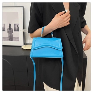 Detail of a bright blue crossbody bag with a wavy flap design and high-gloss finish