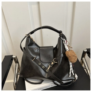 Detail of black faux leather tote with metal eyelets and a cute brown plush bear charm