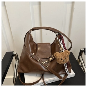Detail of dark brown leather hobo bag with teddy charm and fashion typography on white books