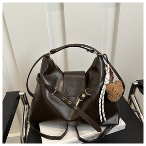 Detail of dark brown leather tote featuring a metal eyelet strap and bear charm
