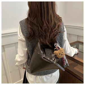 Détail d'un sac porté épaule marron foncé avec œillets métalliques et breloque ourson