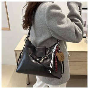Detail of black leather tote bag with decorative metal ring, belt strap and plush bear charm