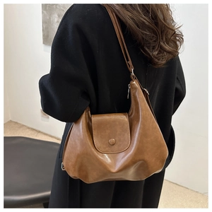 Brown vintage leather tote bag with flap and metal buckle on a black coat back view