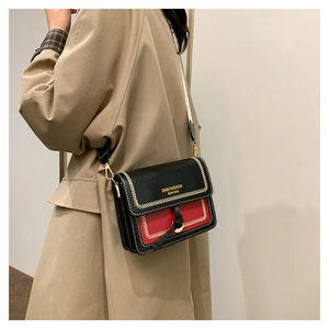 Detail of a black and red crossbody bag with gold embroidery and metal buckle on coat