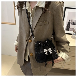 Detail of black drawstring bucket bag with silver bow charm and textured velvet finish