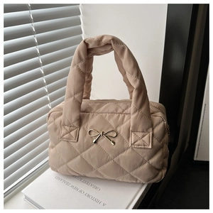 Detail view of khaki quilted handbag with a gold bow accent and wide padded handle