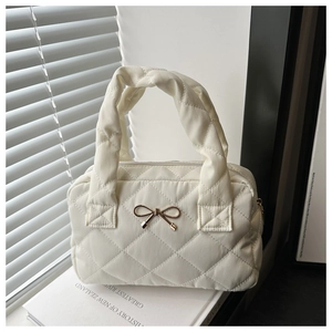 Detail of white quilted tote bag featuring a golden metal bow and zipper closure