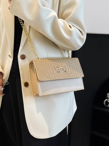 Chic beige woven shoulder bag with gold bow clasp and chain strap on a model