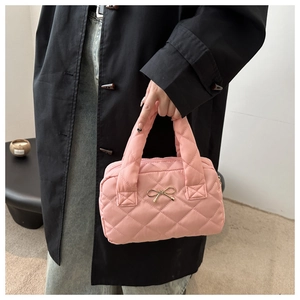 Pink quilted shoulder bag with gold bow detail being held by a model in a minimal setting