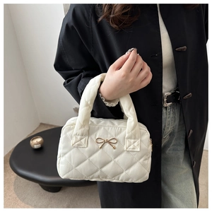 Detail of white quilted bag with golden bow clasp and soft padded texture on the shoulder