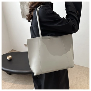 Detail of light grey tote bag showing smooth leather texture and metal logo plaque