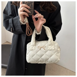 Detail of white quilted nylon handbag featuring a decorative gold metal bow on a black coat