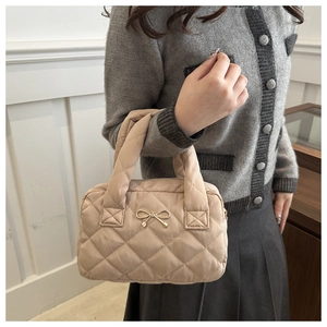 Detail of light beige quilted handbag with golden metal bow and elegant stitching