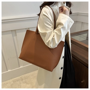 Brown faux leather tote bag worn on shoulder by model in a minimalist studio setting