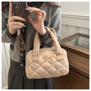 Macro detail of apricot quilted tote bag featuring a golden metal bow and diamond stitching