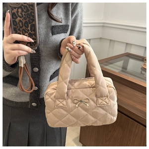 Close-up of beige quilted nylon tote bag featuring a golden metallic bow detail