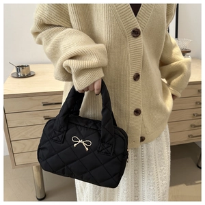 Detail of black quilted handbag with a golden bow pendant and elegant lattice stitching