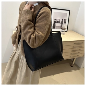 Minimalist black leather tote bag shown on a model in a cozy boutique setting