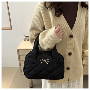 Detail of a black quilted bow tote bag shown with an elegant winter knit outfit