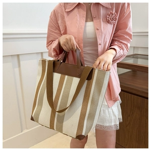 Detail of striped canvas tote bag with brown leather trim and reinforced corner design
