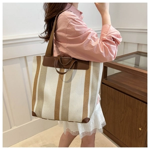 Close-up of canvas striped tote bag with leather trim on model in a minimalist home setting